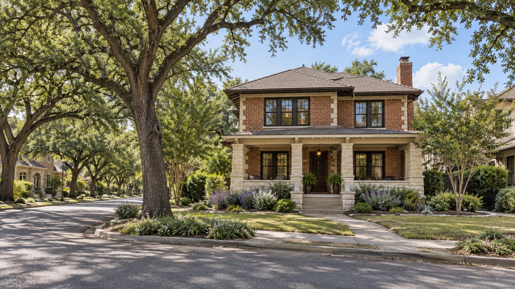 Two-story brick and limestone home with a deep front porch on a street shaded by mature live oaks